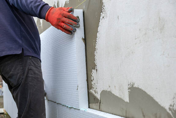Greenwich Insulation's construction worker installing styrofoam insulation sheets on house facade wall for thermal protection.